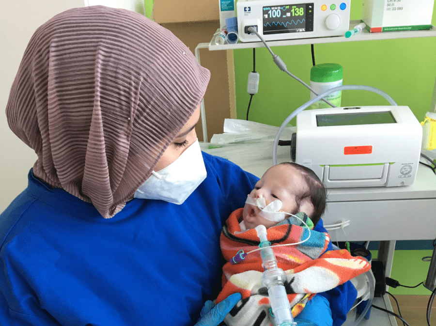 Mutter mit Maske hält beatmetes Baby im Arm