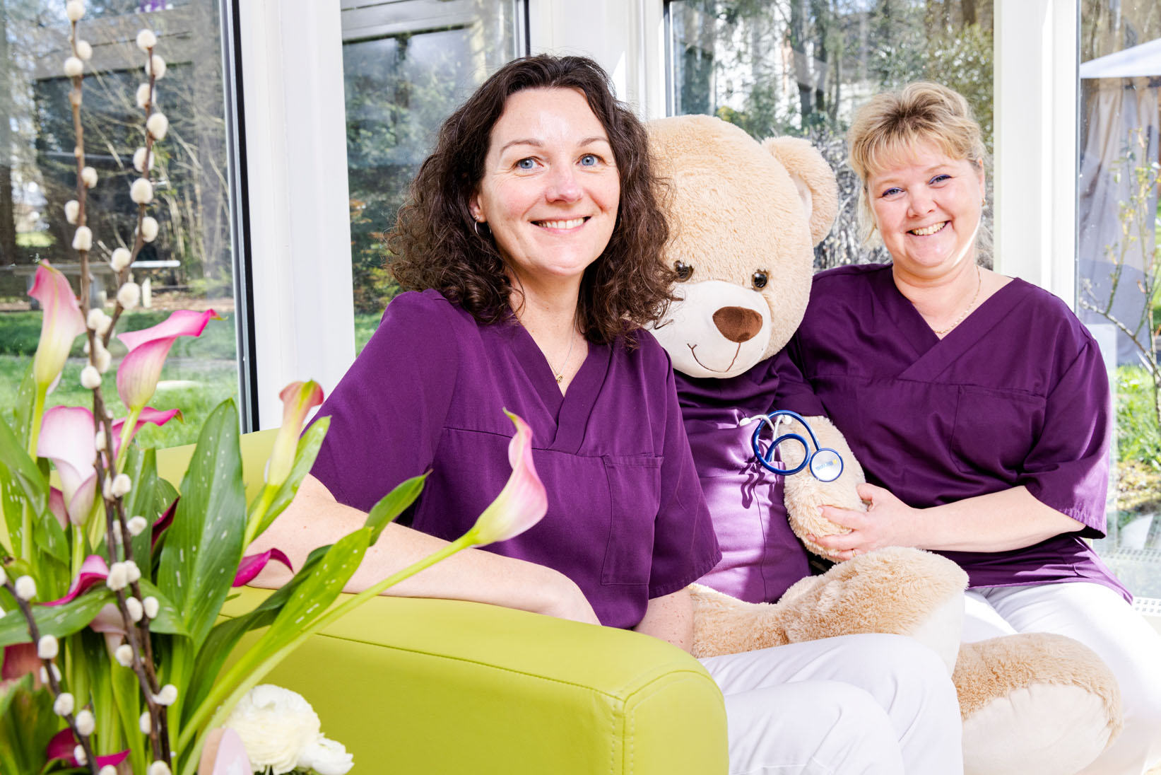 Zwei Pflegefachkräfte auf einem Sofa mit einem Teddybär